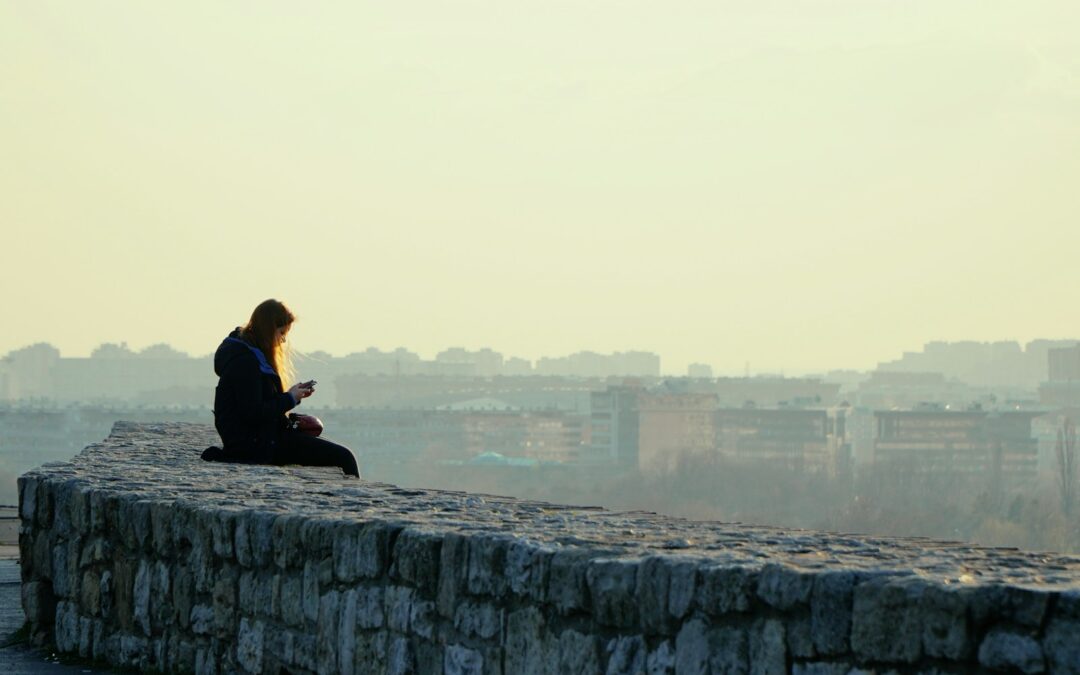 woman in black jacket sitting on gray concrete wall during daytime